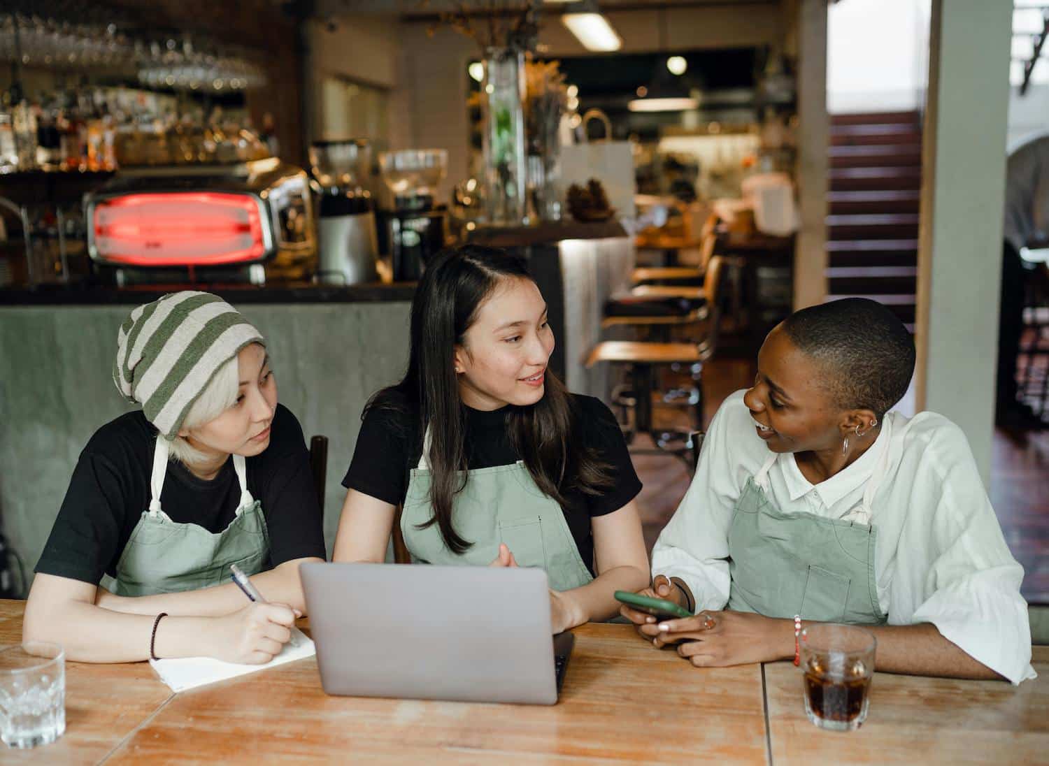Coffee shop employees using their phone and laptop to perform hyperlocal social media marketing.